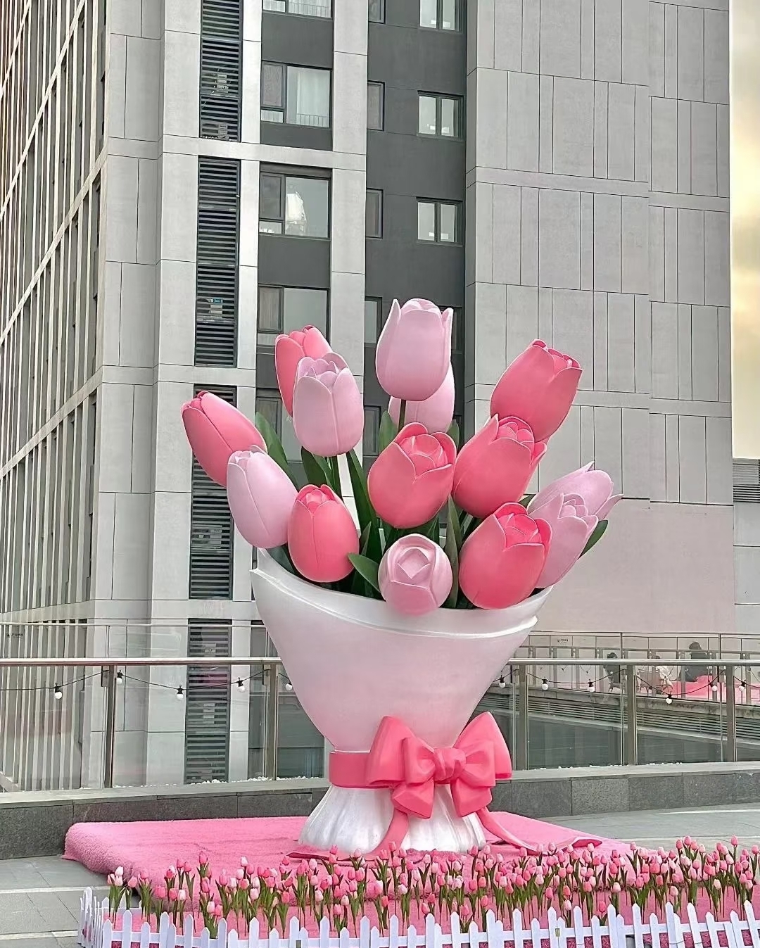 Pink‑white bow‑style fiberglass bouquet sculpture with tulip design as landscape decor on an urban terrace