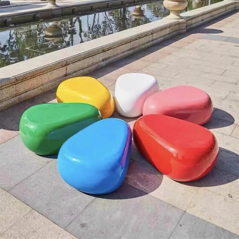 Colorful fiberglass pebble seat set arranged in an outdoor plaza with a fountain background