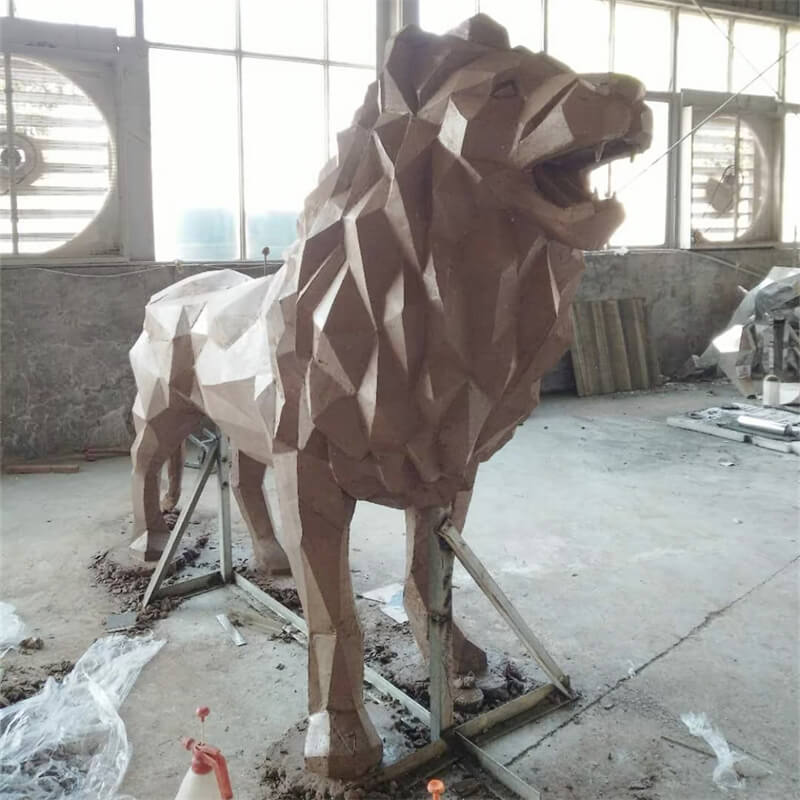 Clay prototype of a fiberglass lion sculpture with geometric cut‑surface craft. A production‑process shot.