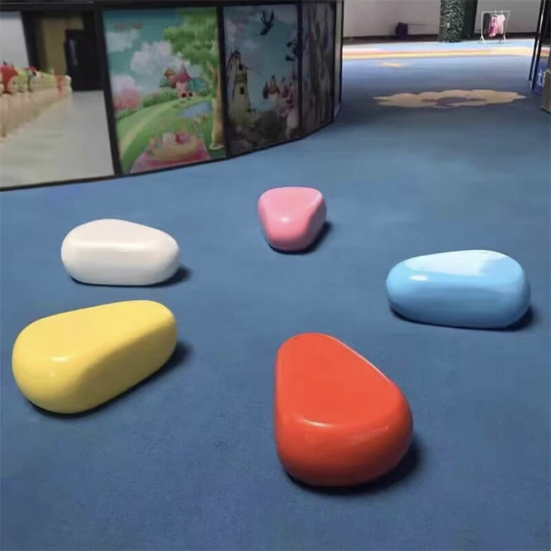Pastel-colored fiberglass pebble seats arranged on a blue carpet in an indoor children's area