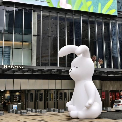 Large white fiberglass rabbit sculpture sitting in front of commercial building, soft matte finish