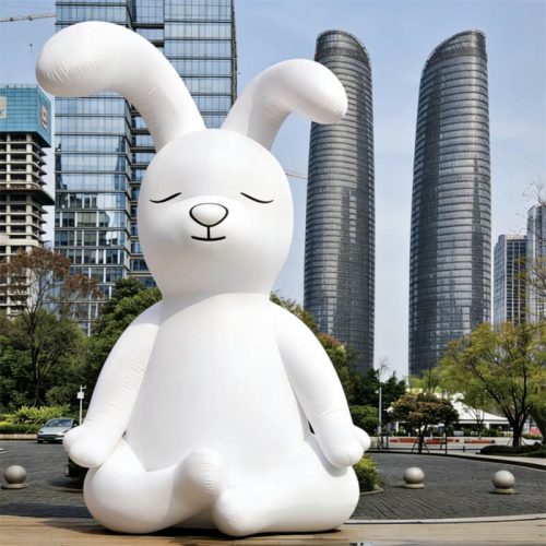 Giant inflatable-style white rabbit sculpture in cross-legged pose, modern city skyscrapers background