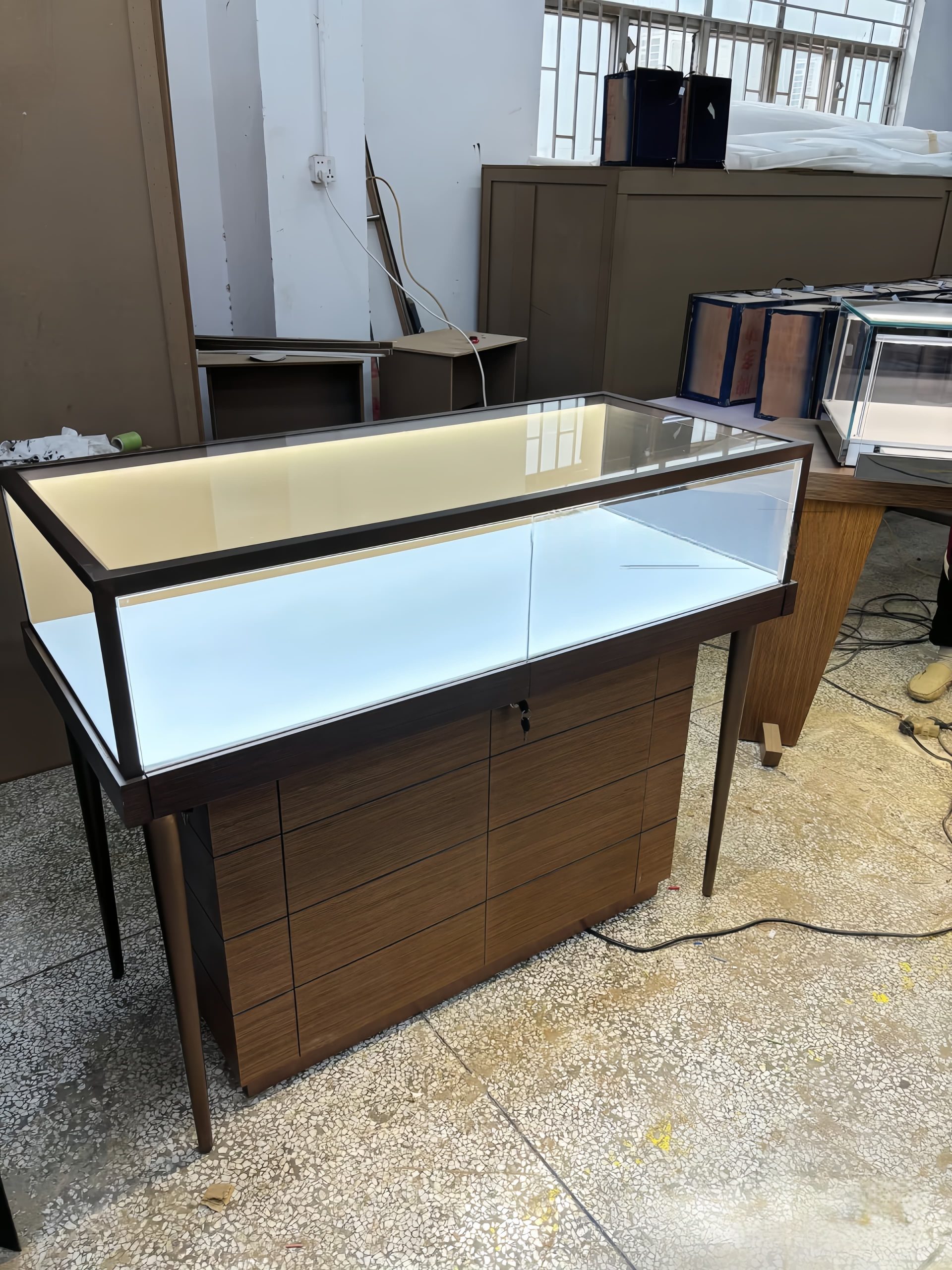 Factory finished walnut jewelry glass display counter with slim black metal legs, LED‑lit glass showcase and drawer storage