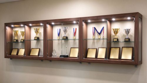 Long wall mounted wooden trophy display case system with glass shelves, left 45 degree view